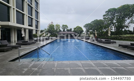 A serene poolside with wicker loungers, closed umbrellas A serene poolside with wicker loungers, closed umbrellas 134497780