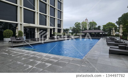 A serene poolside with wicker loungers, closed umbrellas A serene poolside with wicker loungers, closed umbrellas 134497782