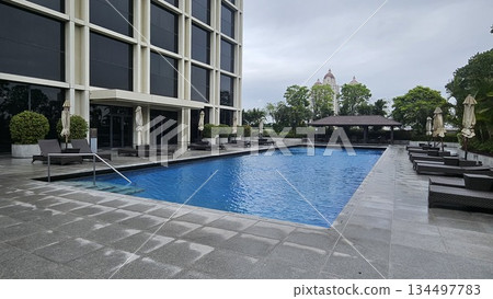 A serene poolside with wicker loungers, closed umbrellas A serene poolside with wicker loungers, closed umbrellas 134497783