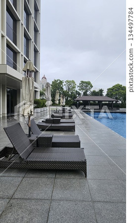 A serene poolside with wicker loungers, closed umbrellas A serene poolside with wicker loungers, closed umbrellas 134497784