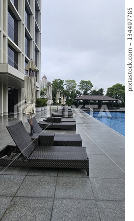 A serene poolside with wicker loungers, closed umbrellas A serene poolside with wicker loungers, closed umbrellas 134497785