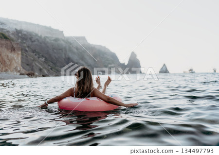 Woman, floating, ocean, relaxing on an inflatable ring near coastal cliffs with copy space. 134497793