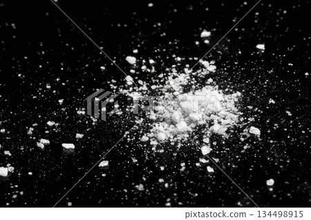 Spilled salt on black surface creates dramatic contrast with scattered white crystals and fine grains, evoking sense of messiness and texture in composition 134498915