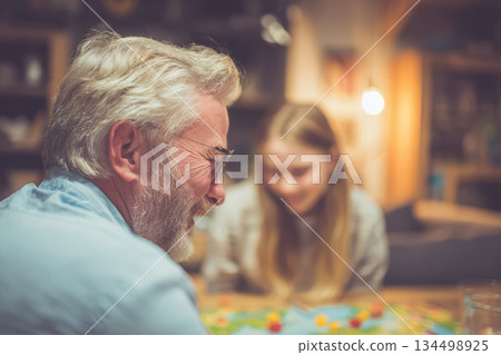 Family enjoying board game night together at home, smiling and having fun in cozy living room with warm lighting, creating happy memories and bonding across generations Family enjoying board game night together at home, smiling and having fun in cozy living room with warm lighting, creating happy memories and bonding across generations 134498925
