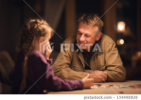 Family board game night brings joy as grandfather and granddaughter share laughter and connection around table in cozy home environment 134498926
