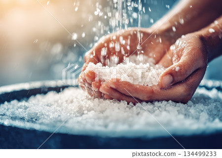Dead sea salt scrub gently falling through hands, creating soothing and relaxing spa atmosphere with natural mineral crystals for skincare and exfoliation 134499233