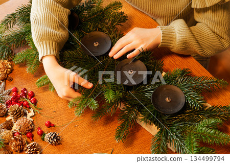 Hands of girl arranging pine branches for advent wreath Hands of girl arranging pine branches for advent wreath 134499794