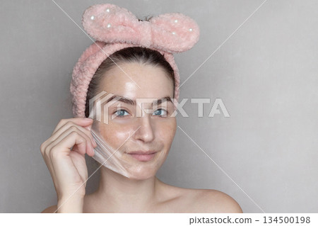 Caucasian woman makes a cosmetic Peel Off Mask. She removes the film mask with her hand copy space photo Caucasian woman makes a cosmetic Peel Off Mask. She removes the film mask with her hand copy space photo 134500198
