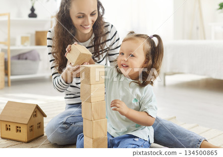 Happy mother and daughter enjoying educational playtime with wooden blocks, building tower together. 134500865