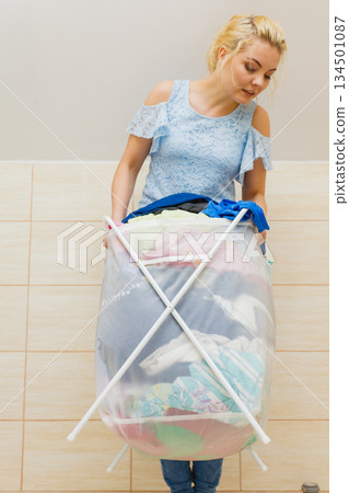 Woman carry big basket of dirty clothes laundry. 134501087