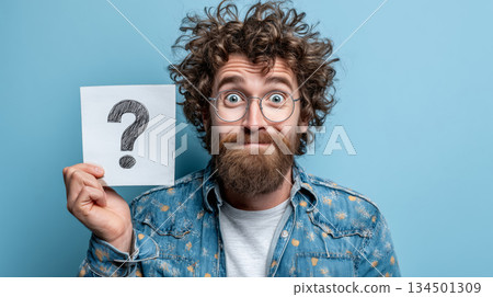 Man with curly hair holding a question mark against a blue background Man with curly hair holding a question mark against a blue background 134501309