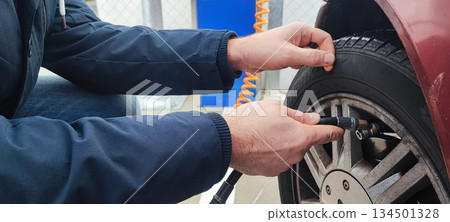 A close-up of an adult's hand inflating a car tire with a compressed air hose at a gas station or garage. Concept: vehicle maintenance, car care, road safety. A close-up of an adult's hand inflating a car tire with a compressed air hose at a gas station or garage. Concept: vehicle maintenance, car care, road safety. 134501328