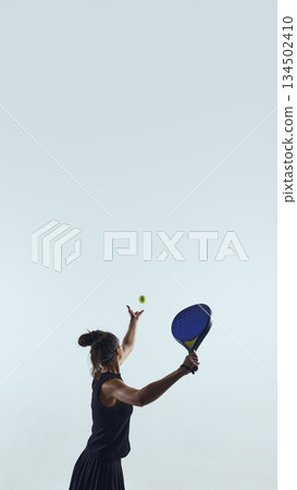 Female padel athlete tosses ball preparing overhead serve. Female padel athlete tosses ball preparing overhead serve. 134502410