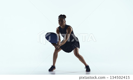 Female padel player prepares to receive the ball in minimalist studio space 134502415