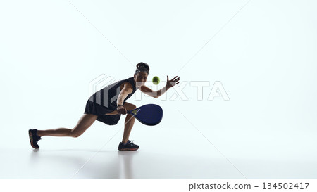 Female padel player moving forward and reaching ball in studio. Female padel player moving forward and reaching ball in studio. 134502417