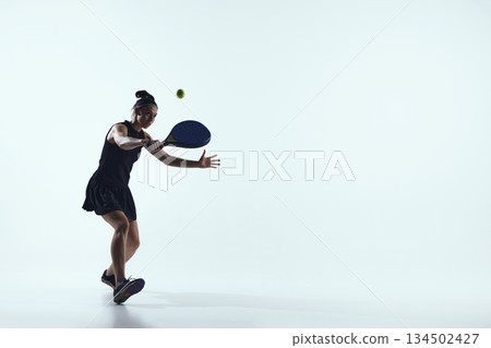 Female padel player controlled backhand shot on white background. Female padel player controlled backhand shot on white background. 134502427