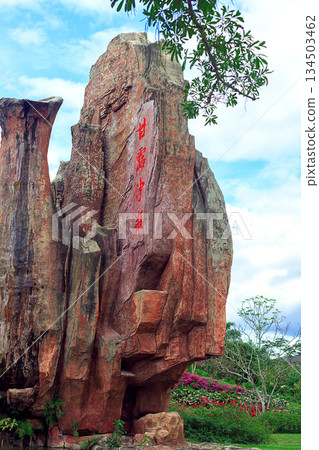 A tall rock face with vertical Chinese character carvings in Nanshan Tropical Park. 134503462