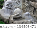 A stone sculpture of a sage against a backdrop of cliffs and greenery at the Heavenly Grottoes Park, Hainan. 134503471