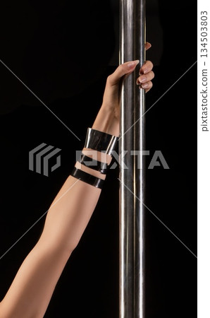 Arm with black cuffs grips metal pole in a studio with a black background 134503803