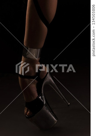 Dancer wears high heel platform shoes with ankle strap in dark studio during dance performance 134503806