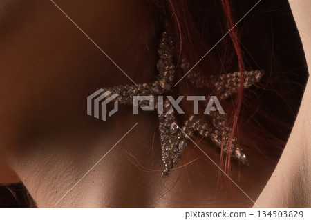 Close-up of woman wearing a sparkly star earring with auburn hair 134503829