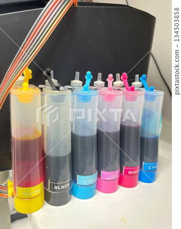 A printer with six ink cartridges in various colors and levels on a white surface, great for printing supply ads, home office equipment shots, and color management tutorials. 134503858