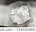 A container filled with crumpled receipts on a flat surface, perfect for tax season visuals, expense tracking content, and office financial organization themes. 134503860