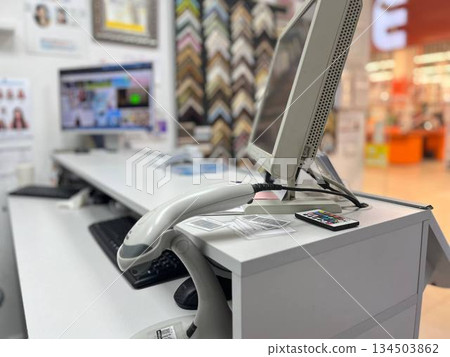 A desk with a computer monitor, keyboard, and barcode scanner against shelves with pictures, perfect for home office setups, inventory management themes, and organized workspace photography. 134503862