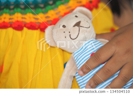 Child holds teddy bear in colorful dress Child holds teddy bear in colorful dress 134504510