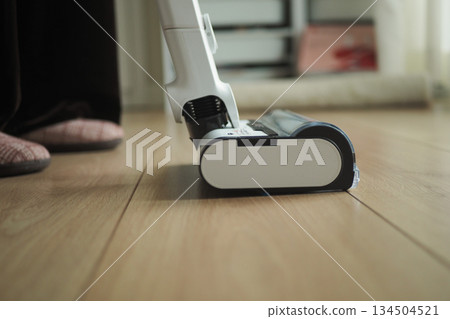 Person vacuums floor at home during day 134504521