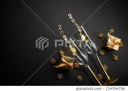 New Year Celebration 2026. Champagne glasses with 2026 toppers and gift boxes on a dark backdrop. 134504706