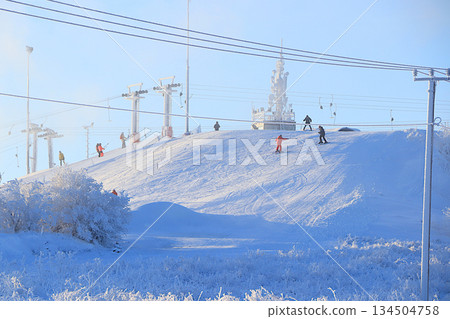 Ski lifts at the Tuutari Park mountain ski resort in the Leningrad region, covered with a thick layer of ice and skiers riding on the slope.Winter landscape in central Russia. Ski lifts at the Tuutari Park mountain ski resort in the Leningrad region, covered with a thick layer of ice and skiers riding on the slope.Winter landscape in central Russia. 134504758