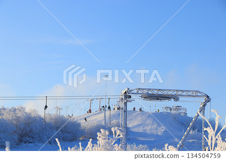 Ski lifts at the Tuutari Park mountain ski resort in the Leningrad region, covered with a thick layer of ice and skiers riding on the slope.Winter landscape in central Russia. Ski lifts at the Tuutari Park mountain ski resort in the Leningrad region, covered with a thick layer of ice and skiers riding on the slope.Winter landscape in central Russia. 134504759