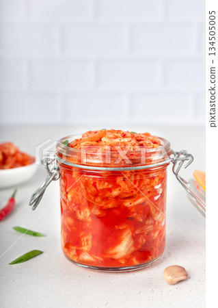 Glass jar with Korean kimchi on white kitchen. Spicy fermented cabbage with chili and garlic. Probiotic food. Copy space 134505005
