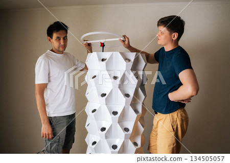 Portrait of two urban farmer working together on vertical hydroponic tower, integrating cutting-edge technology with sustainable agriculture for innovative indoor food growing techniques. Portrait of two urban farmer working together on vertical hydroponic tower, integrating cutting-edge technology with sustainable agriculture for innovative indoor food growing techniques. 134505057