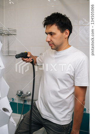 Vertical shot of gardener male sanitizing vertical hydroponic tower garden with steam cleaner in bathroom, highlighting innovative indoor gardening and cleaning technique. Concept of home gardening. Vertical shot of gardener male sanitizing vertical hydroponic tower garden with steam cleaner in bathroom, highlighting innovative indoor gardening and cleaning technique. Concept of home gardening. 134505066