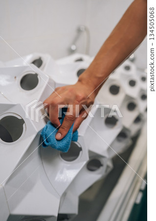 Vertical cropped shot of man wiping white hydroponic system with blue cloth, maintaining pristine growing environment for thriving indoor plants with sustainable cultivation techniques. Vertical cropped shot of man wiping white hydroponic system with blue cloth, maintaining pristine growing environment for thriving indoor plants with sustainable cultivation techniques. 134505068