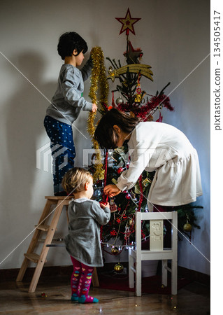 three children decorating christmas tree together at home three children decorating christmas tree together at home 134505417