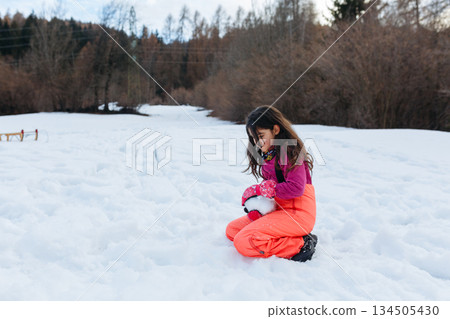 one girl sitting on the snow and making snow ball 134505430