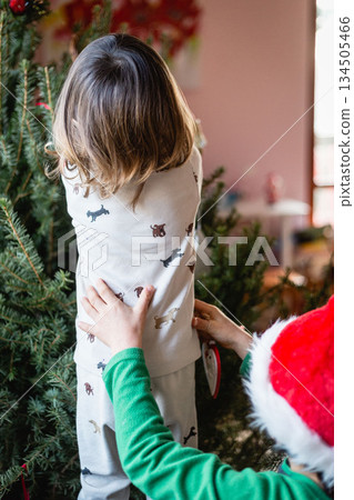 back view of baby decorating christmas tree at home 134505466