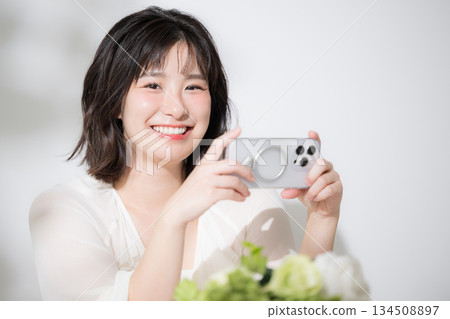 開心又愉悅地看著智慧型手機。一位可愛的年輕女子麵帶微笑,近距離觀看手機上的視頻,目光看向鏡頭。 開心又愉悅地看著智慧型手機。一位可愛的年輕女子麵帶微笑,近距離觀看手機上的視頻,目光看向鏡頭。 134508897