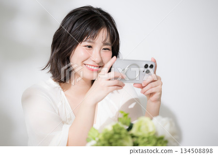 開心又有趣的看著智慧型手機。特寫鏡頭:一位可愛的年輕女子麵帶微笑,正在用智慧型手機觀看影片。 開心又有趣的看著智慧型手機。特寫鏡頭:一位可愛的年輕女子麵帶微笑,正在用智慧型手機觀看影片。 134508898
