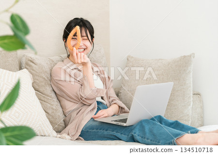 一位年輕的亞裔女性坐在客廳的沙發上吃甜甜圈。 134510718