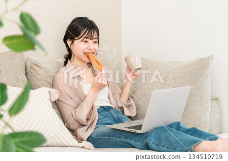 Young Asian woman sitting on a sofa in the living room and eating a donut Young Asian woman sitting on a sofa in the living room and eating a donut 134510719