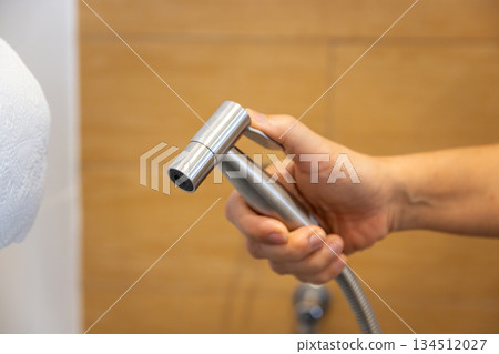 Woman is holding a stainless steel handheld bidet sprayer in bathroom. Woman is holding a stainless steel handheld bidet sprayer in bathroom. 134512027