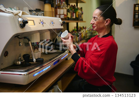 A Hispanic, middle-aged cafe owner in a red sweater crafts coffee at a busy espresso machine, conveying warmth, hospitality, and the daily bustle of a small family-owned cafe. 134513123