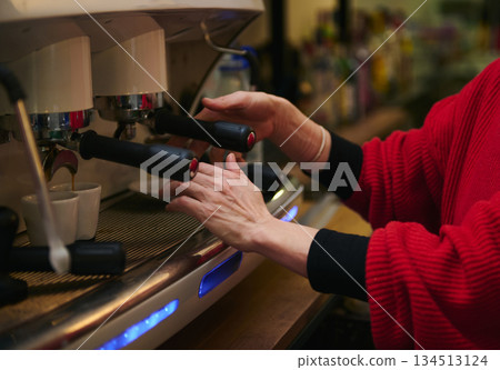 A Hispanic cafe owner tends an espresso machine, skillfully pulling shots as steam rises. Warm, welcoming atmosphere highlighting hospitality, small business and daily cafe routine. 134513124