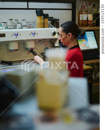 A Hispanic, middle-aged cafe owner operates a professional espresso machine in a warm, inviting shop. The scene highlights hospitality, small business, and daily coffee craftsmanship. 134513130