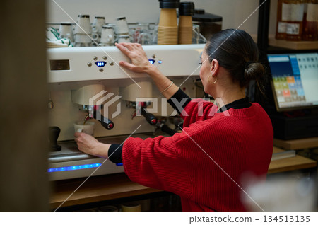 A Hispanic woman cafe owner operates a professional espresso machine, preparing cups in a cozy cafe. Emphasizes hospitality, small business, and daily coffee service. A Hispanic woman cafe owner operates a professional espresso machine, preparing cups in a cozy cafe. Emphasizes hospitality, small business, and daily coffee service. 134513135