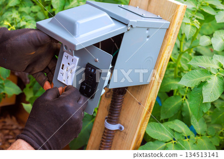 Worker installs electrical outlet in garden to enhance power access for tools equipment Worker installs electrical outlet in garden to enhance power access for tools equipment 134513141
